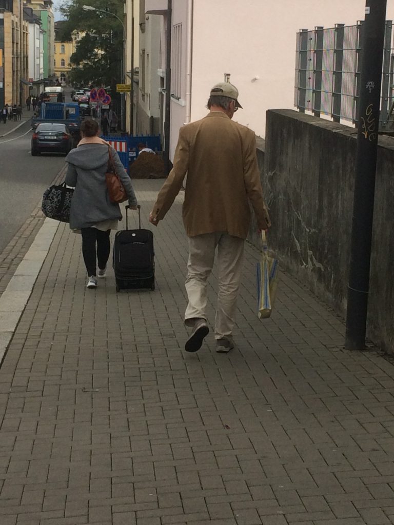 Bürgersteig mit einem Herren in beigen Jacket und Einkaufstasche